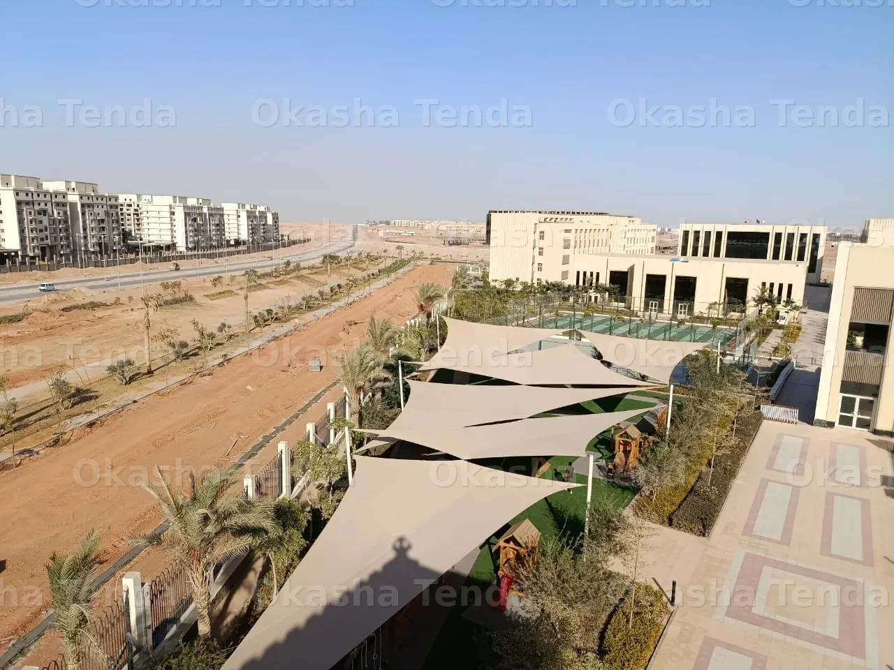 مظلات قماش كبيرة مثبتة على أعمدة معدنية في منطقة سكنية مفتوحة مع نباتات وممرات حجرية.