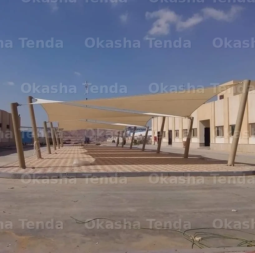 مظلات خارجية قماشية بأعمدة مائلة لتوفير الظل في ساحة مفتوحة بجانب مباني