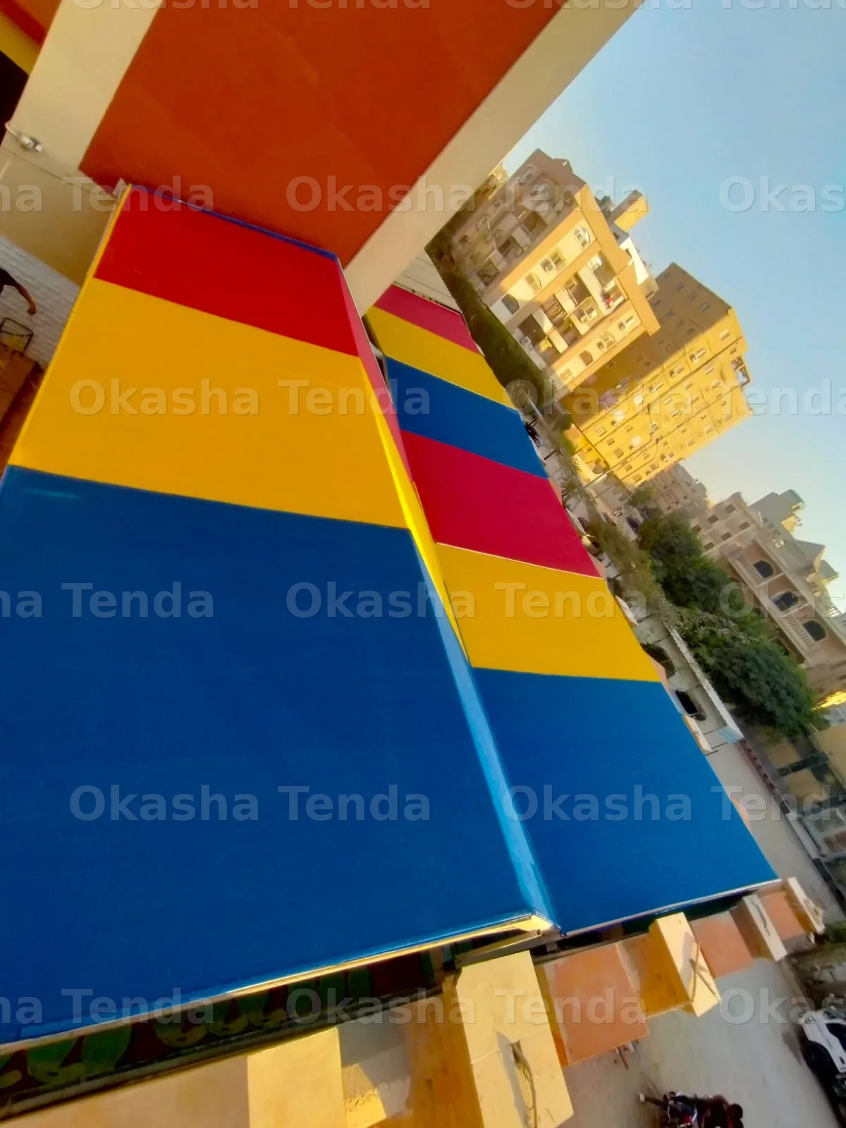 سقفين مغطين بأقمشة ملونة باللون الأزرق والأصفر والأحمر فوق ساحة بين المباني