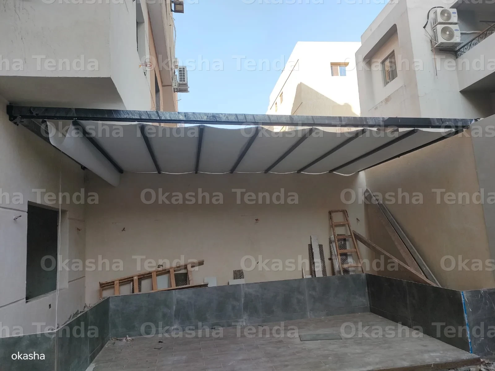 تند قماش أبيض قابل للسحب مثبت بألواح معدنية سوداء بين جدران مبنى سكني في فناء خارجي